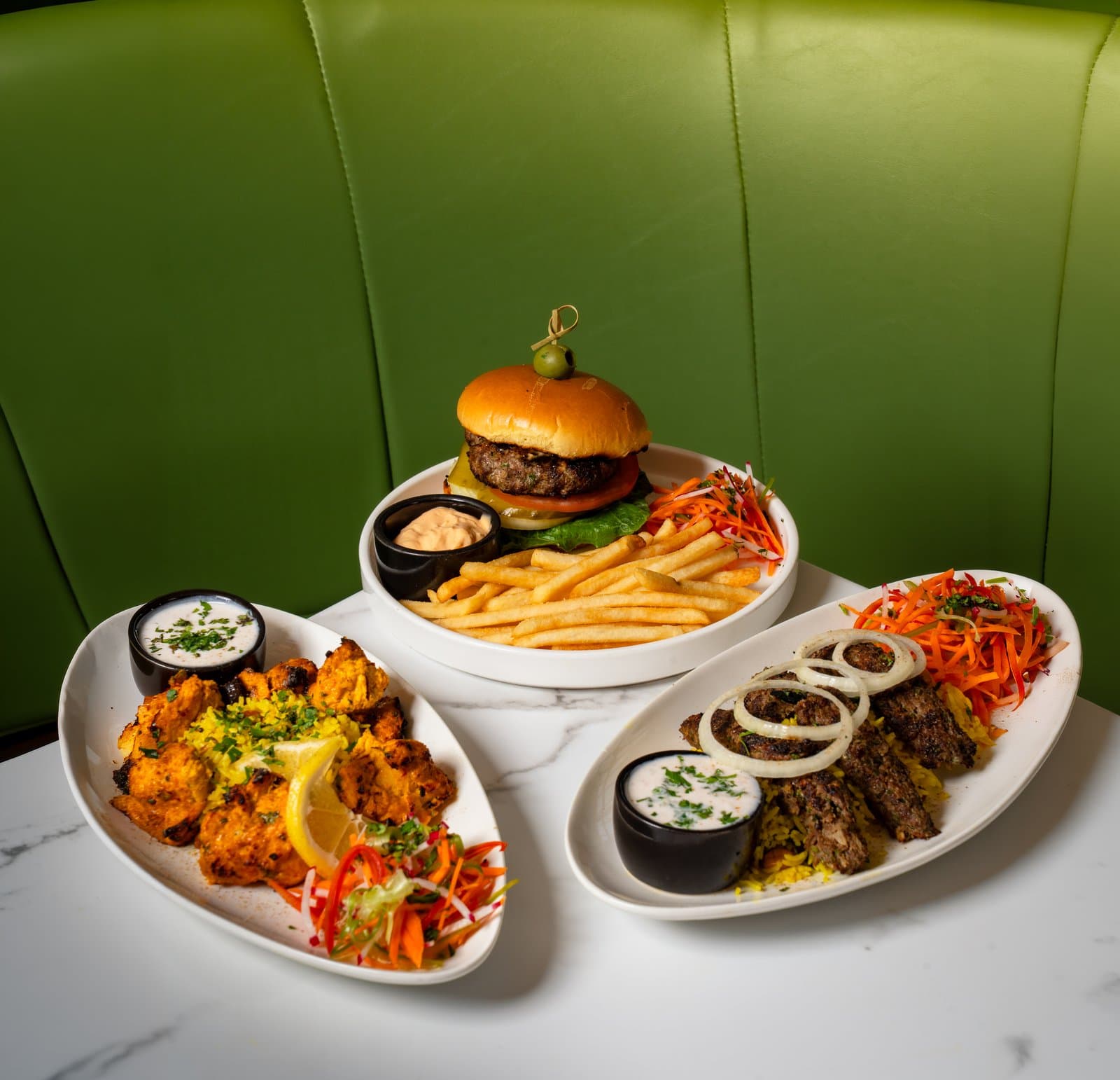 Three plated dishes on a marble table against a green banquette